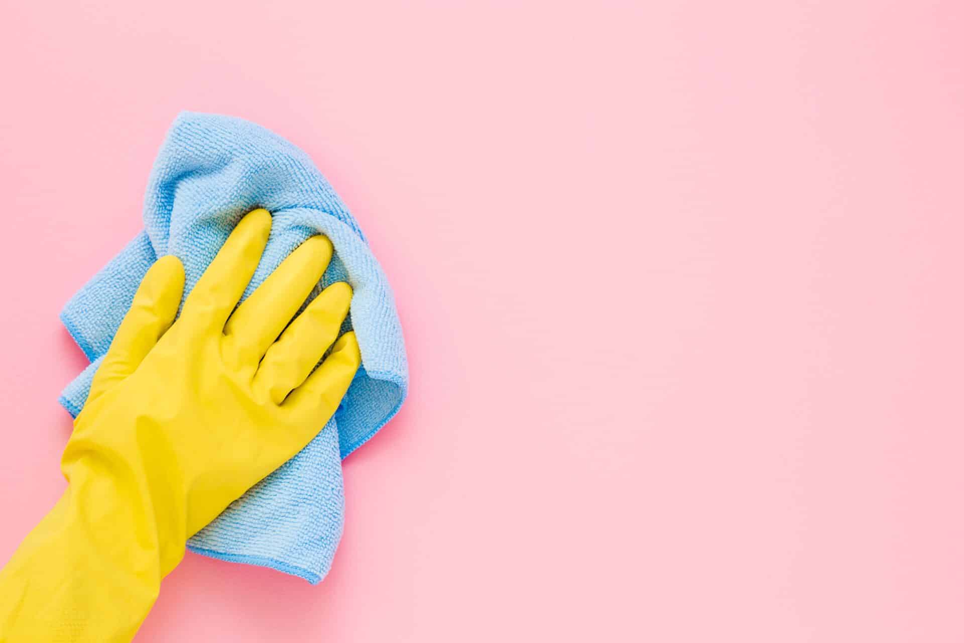Hand In Yellow Rubber Protective Glove Wiping Pastel Pink Wall From Dust With Blue Dry Rag